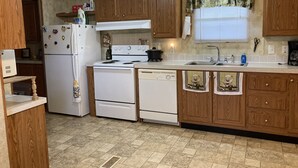 A kitchen with wooden cabinets, a white stove, a dishwasher, and a window with blinds. - Quiet secluded private single wide mobile home  (Jasper)