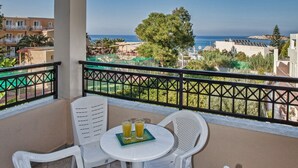 Un balcón con mesa y sillas, con vistas a la costa y edificios, y un árbol.