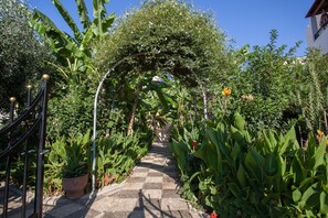 Un sendero en el jardín con diseño de tablero de ajedrez que lleva a una zona cubierta con plantas y flores.