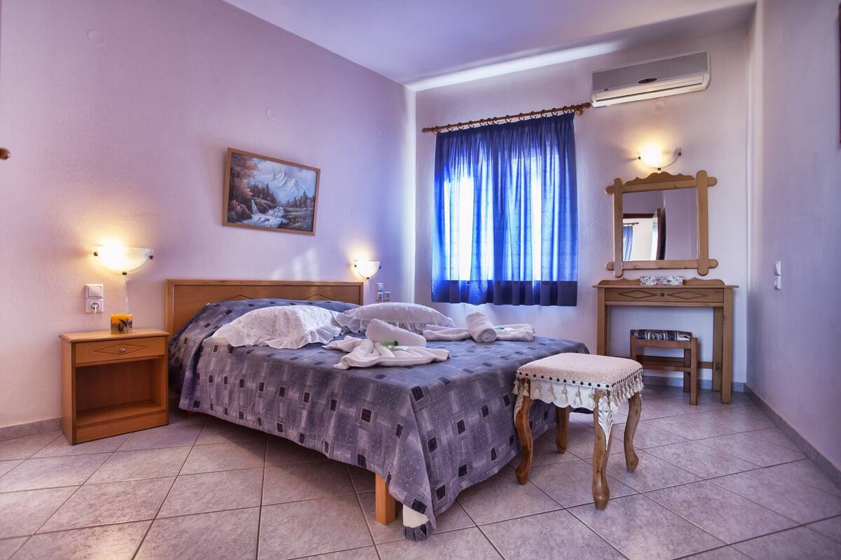 A bedroom with a bed, nightstands, a small table, a mirror, and a window with curtains.