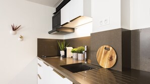 A modern kitchen with a black sink, stainless steel faucet, and a wooden cutting board. - My Nest Inn Marais - 5 pers- 53m² - Heart of Paris (Paris)