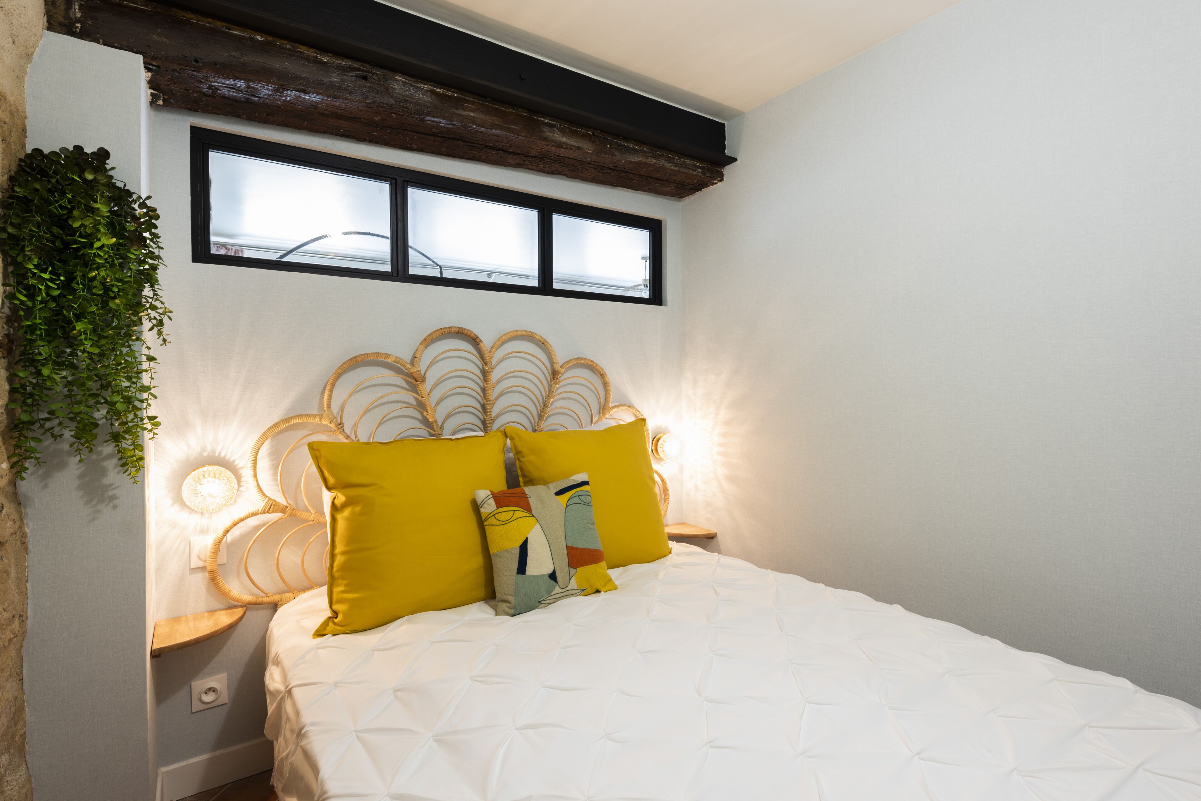 Une chambre à coucher comprenant un lit, deux tables de chevet, une fenêtre et un luminaire fixé au mur.