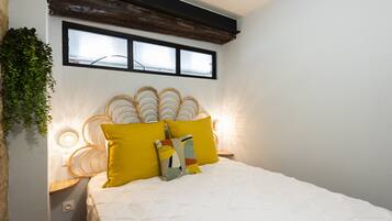 Une chambre à coucher comprenant un lit, deux tables de chevet, une fenêtre et un luminaire fixé au mur.