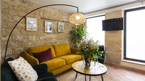 A living room with a yellow sofa, a green armchair, a round coffee table, a large plant, and a wall-mounted TV. - My Nest Inn Marais - 5 pers- 53m² - Heart of Paris (Paris)