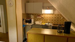 Cocina compacta con microondas, estufa y lavamanos. Un reloj se ve en la pared.