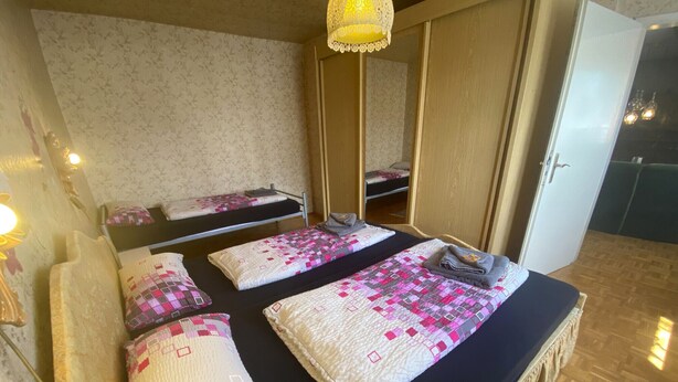 Habitación con dos camas, cada una con colcha y almohadas, un espejo y suelo de madera.