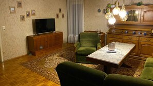 Una sala de estar con televisor, sillón verde, aparador de madera y alfombra estampada.