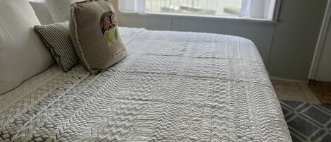 Una cama bien hecha con un edredón estampado y varias almohadas, incluyendo una con un parche.
