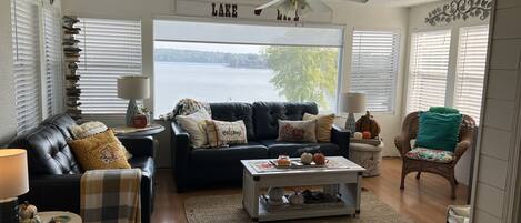 A cozy living room with a black leather sofa, a coffee table, and a view of a lake.
