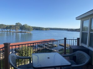 A balcony with a table and chairs overlooking a lake, with a view of a dock and a distant shoreline. - Vintage Lake Front Cottage, thoughtful updates, cleaned and cared for by owner (Hot Springs)
