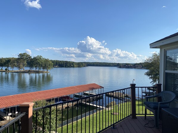 A lakeside deck with a red roof, a grassy area, and a view of the lake and distant trees. - Vintage Lake Front Cottage, thoughtful updates, cleaned and cared for by owner (Hot Springs)