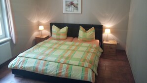 Un dormitorio con una cama, dos mesitas de noche con lámparas, una ventana con cortinas y un cuadro en la pared.