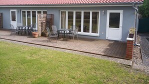 Una casa con techo de tejas rojas, ventanas grandes y un patio con mobiliario exterior.
