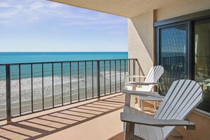 Ein Balkon mit Blick auf den Strand, eine Glastür und ein weißer Stuhl.
