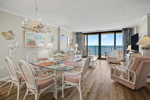 Ein geräumiger Wohnbereich mit einem Glastisch, Korbstühlen, einer Couch und einem Balkon mit Meerblick.