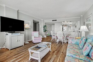 A living room with a flat-screen TV, white furniture, a pink armchair, and a floral sofa.