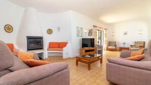 Una sala de estar con chimenea, sofás naranja y grises, una mesa de centro de madera y un televisor.