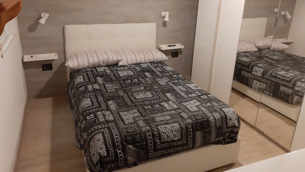 Una camera da letto con un letto, un comodino, una lampada a parete e uno specchio.