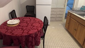Una cocina compacta con una mesa de comedor cubierta por un mantel rojo, un refrigerador blanco y un armario de madera.