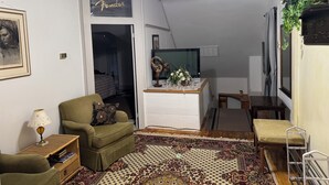 Una sala de estar con un sofá, una mesita con una lámpara, un ventilador de techo, un televisor sobre un mueble bajo y una alfombra estampada.