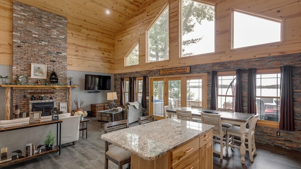 Une cuisine spacieuse dotée d’un grand îlot central, d’un plafond en bois et de grandes fenêtres donnant sur un lac.