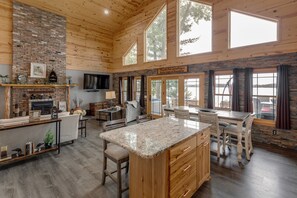 A spacious kitchen with a large island, wooden ceiling, and large windows overlooking a lake.