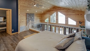 Une chambre dotée d’un grand lit, d’un plafond en bois et offrant une vue sur l’extérieur grâce à de grandes fenêtres.