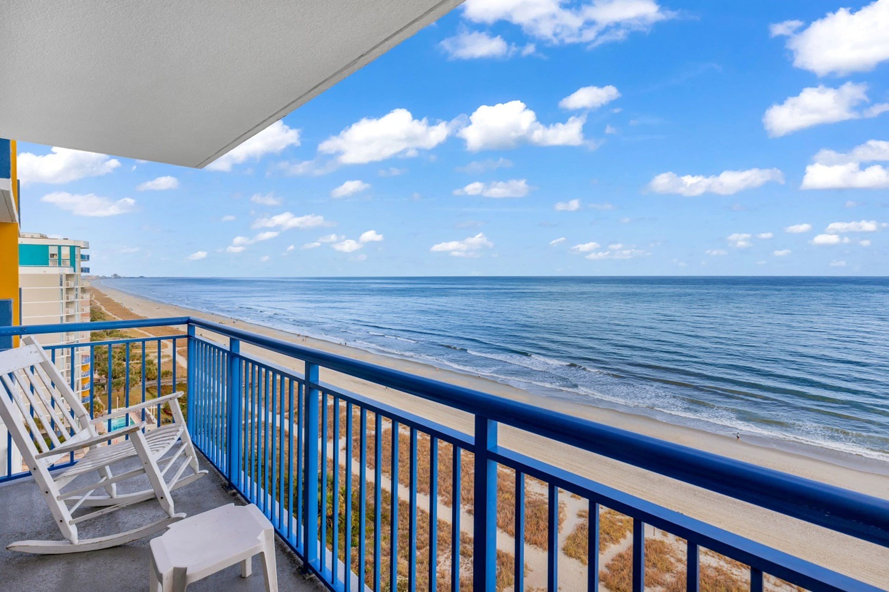A balcony with a view of the ocean, a white rocking chair, and a small table.