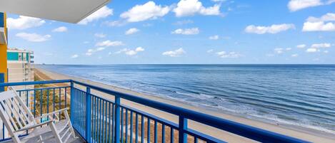 A balcony with a view of the ocean, a white rocking chair, and a small table.
