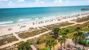 A beach with umbrellas, lounge chairs, and a pier. - Stunning Oceanfront View Atlantica Tower (Myrtle Beach)