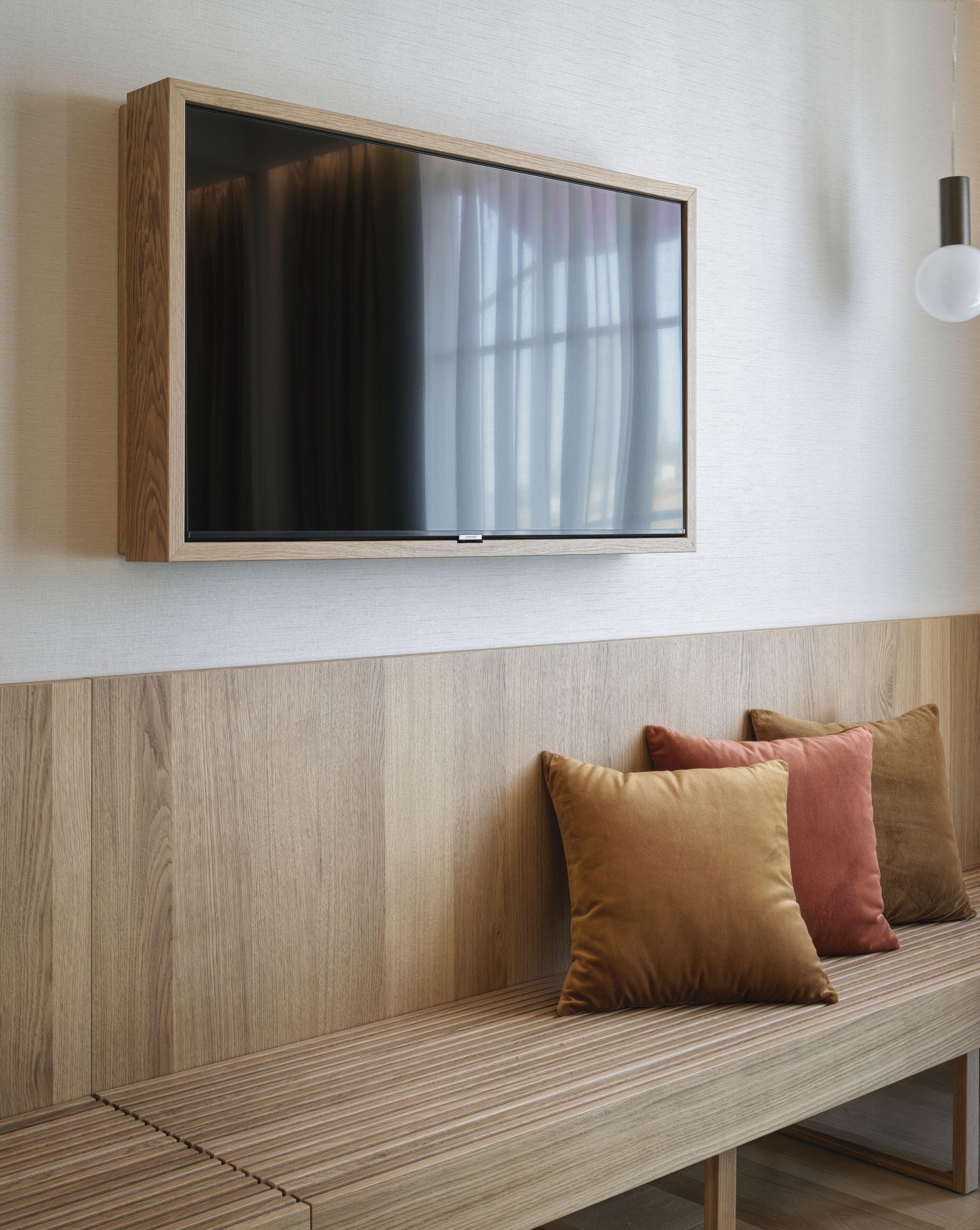 Una sala de estar moderna con un banco de madera, un televisor de pantalla plana montado y una lámpara.