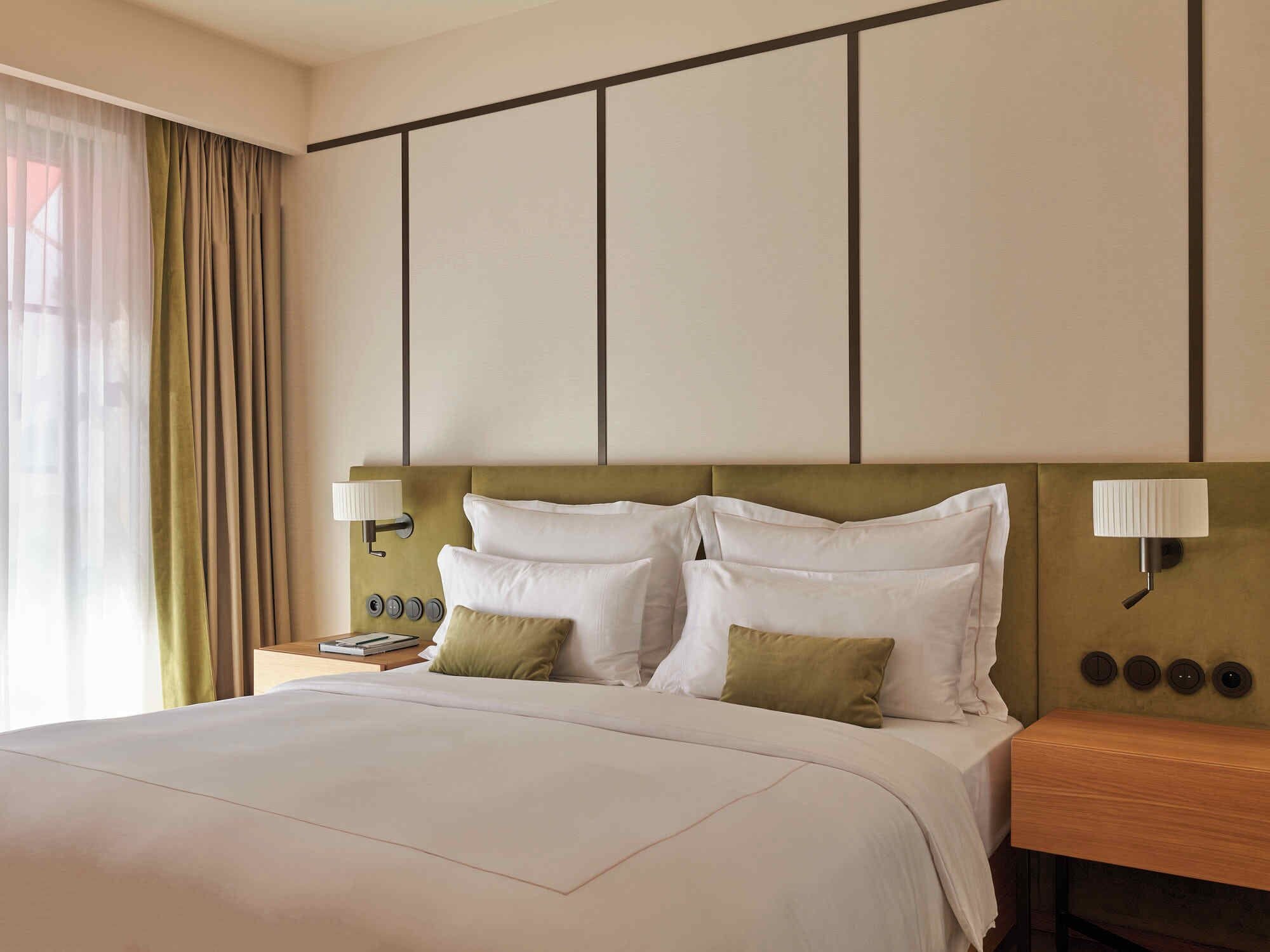 Een hotelkamer met een groot bed, twee nachtkastjes en een wandlamp.