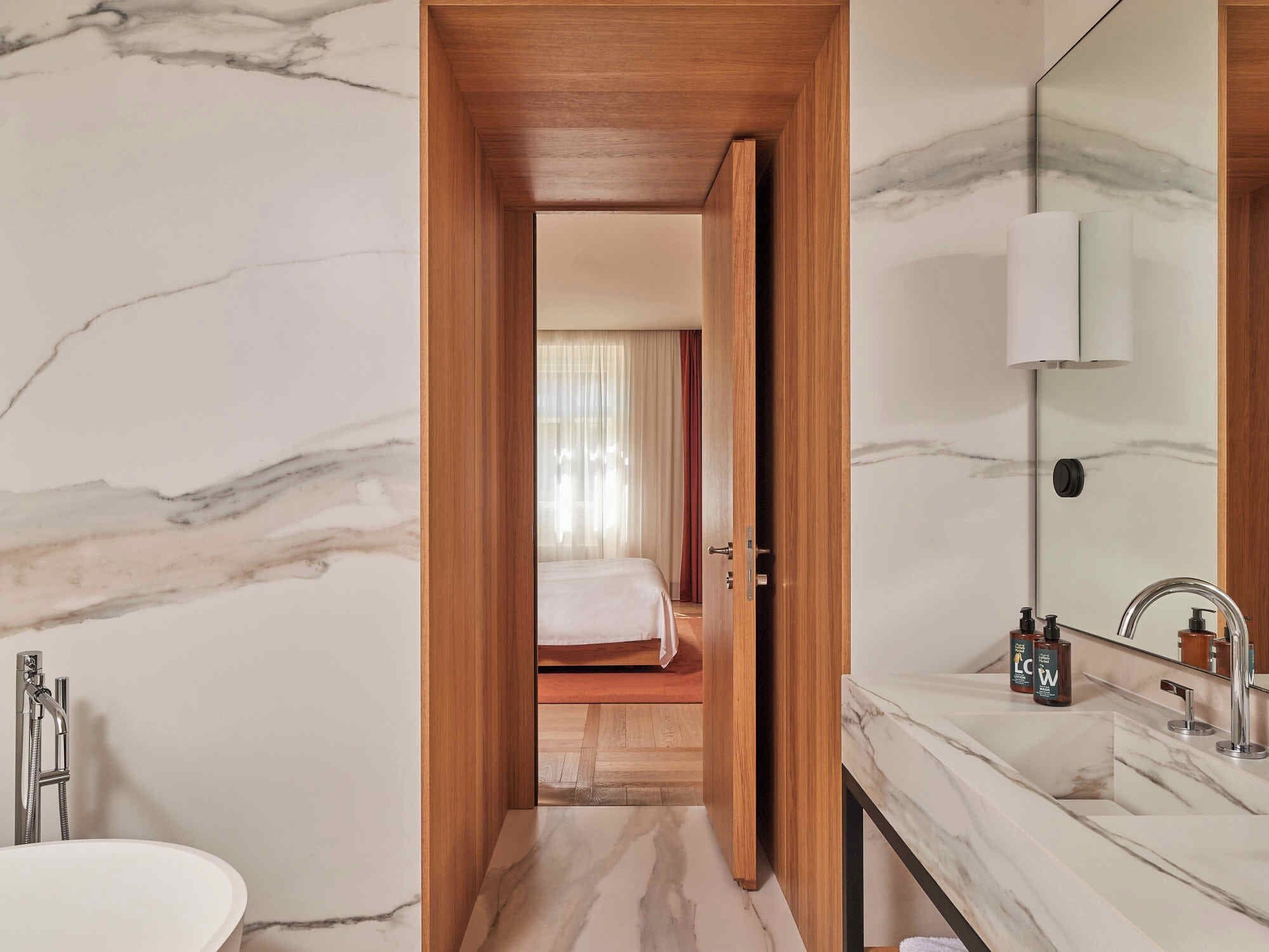 Um banheiro moderno com uma pia de mármore, uma porta de madeira que dá para um quarto e um espelho grande.