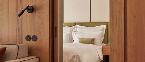 Una habitación de hotel con una puerta de madera, una cama con ropa blanca y un sofá color beige.
