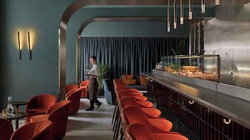 Un espace bar moderne avec des chaises à revêtement rouge, un comptoir en acier inoxydable et des luminaires suspendus.