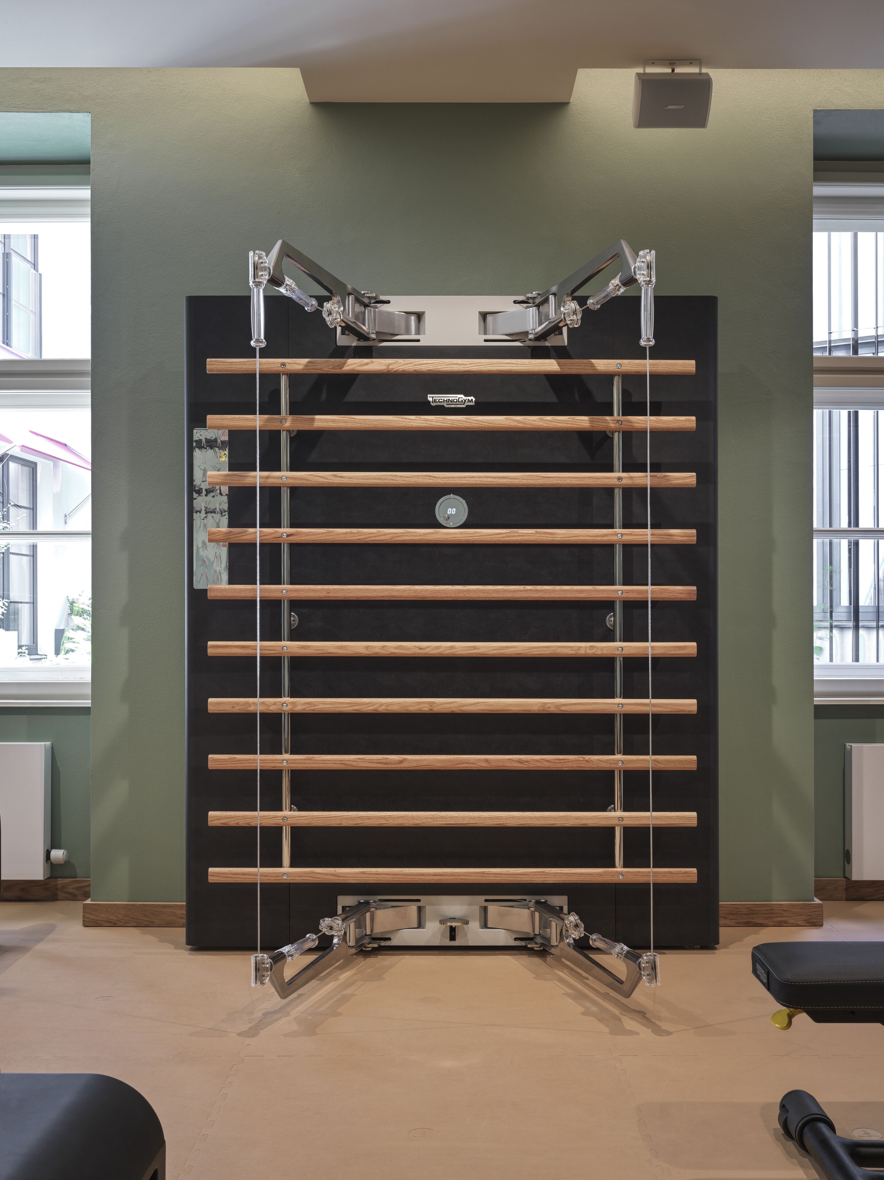 Un gimnasio con una estructura de barra para dominadas, un panel de control y una ventana con vistas a edificios.