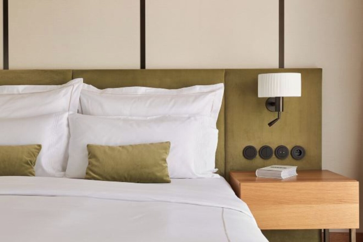 A neatly made bed with white and green pillows, a wooden nightstand with a lamp, and a book.