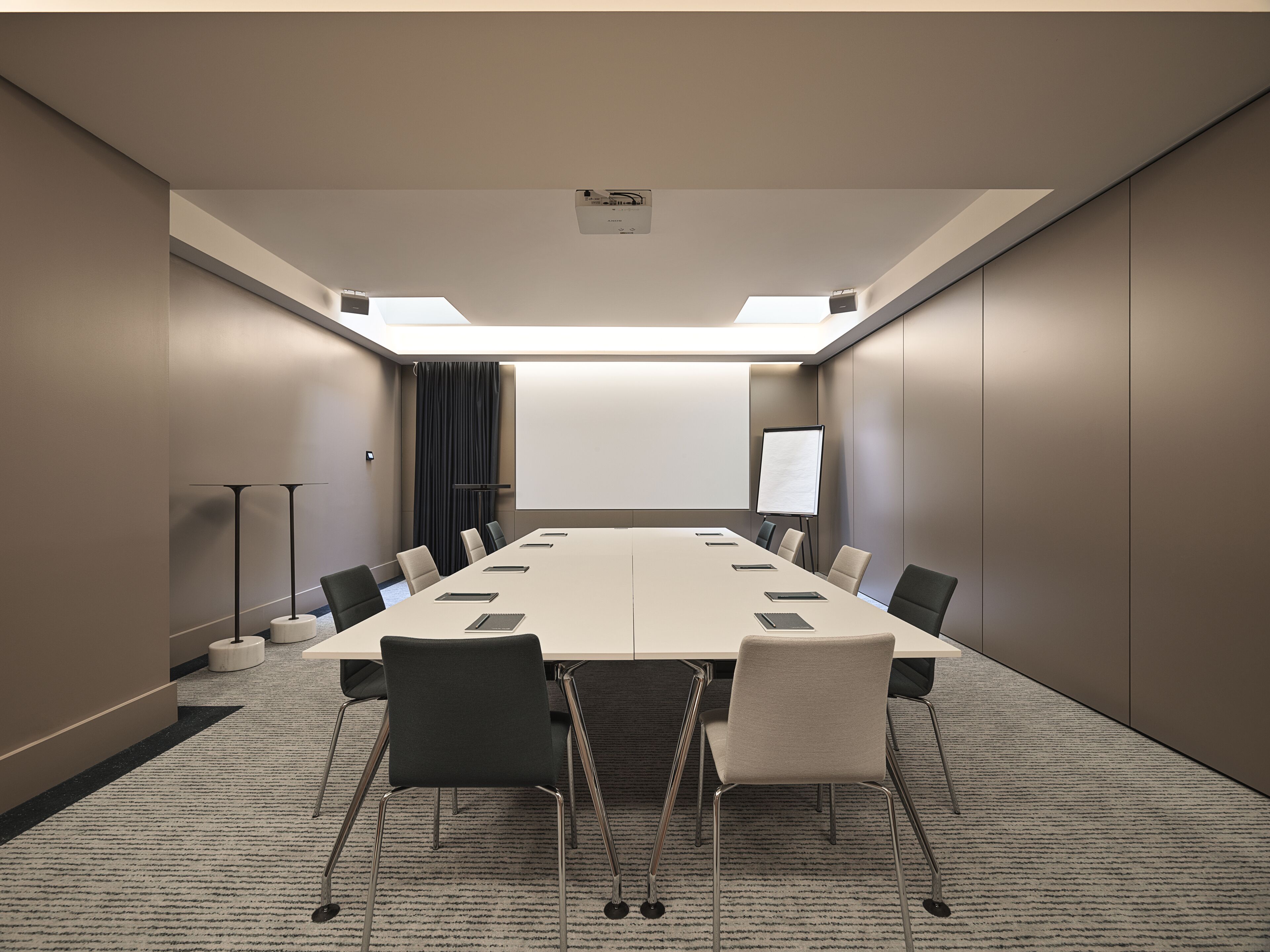 Uma sala de conferência com uma mesa comprida, cadeiras, uma tela de projetor e uma lousa.