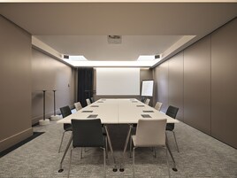 Uma sala de conferência com uma mesa comprida, cadeiras, uma tela de projetor e uma lousa.