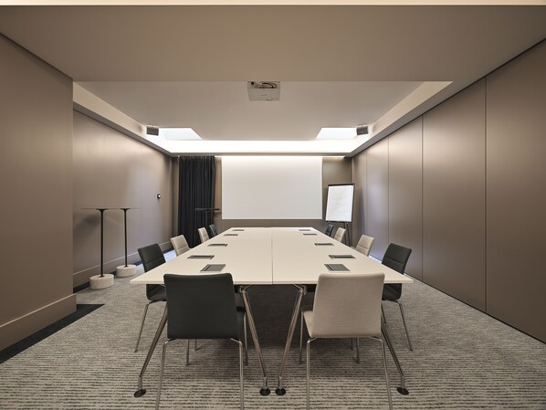 A conference room with a long table, chairs, a projector screen, and a whiteboard.