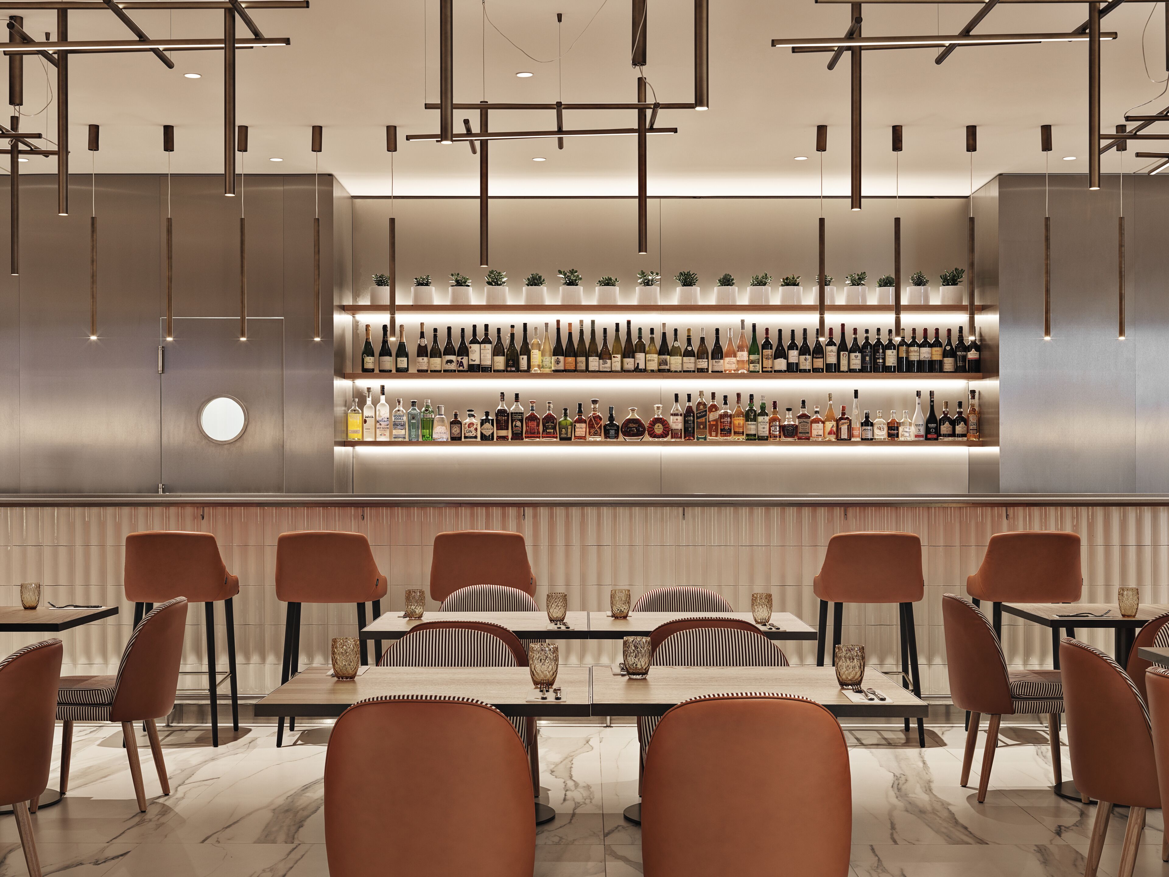 Una zona de bar moderna con una variedad de botellas de licor, taburetes de bar elegantes e iluminación contemporánea.
