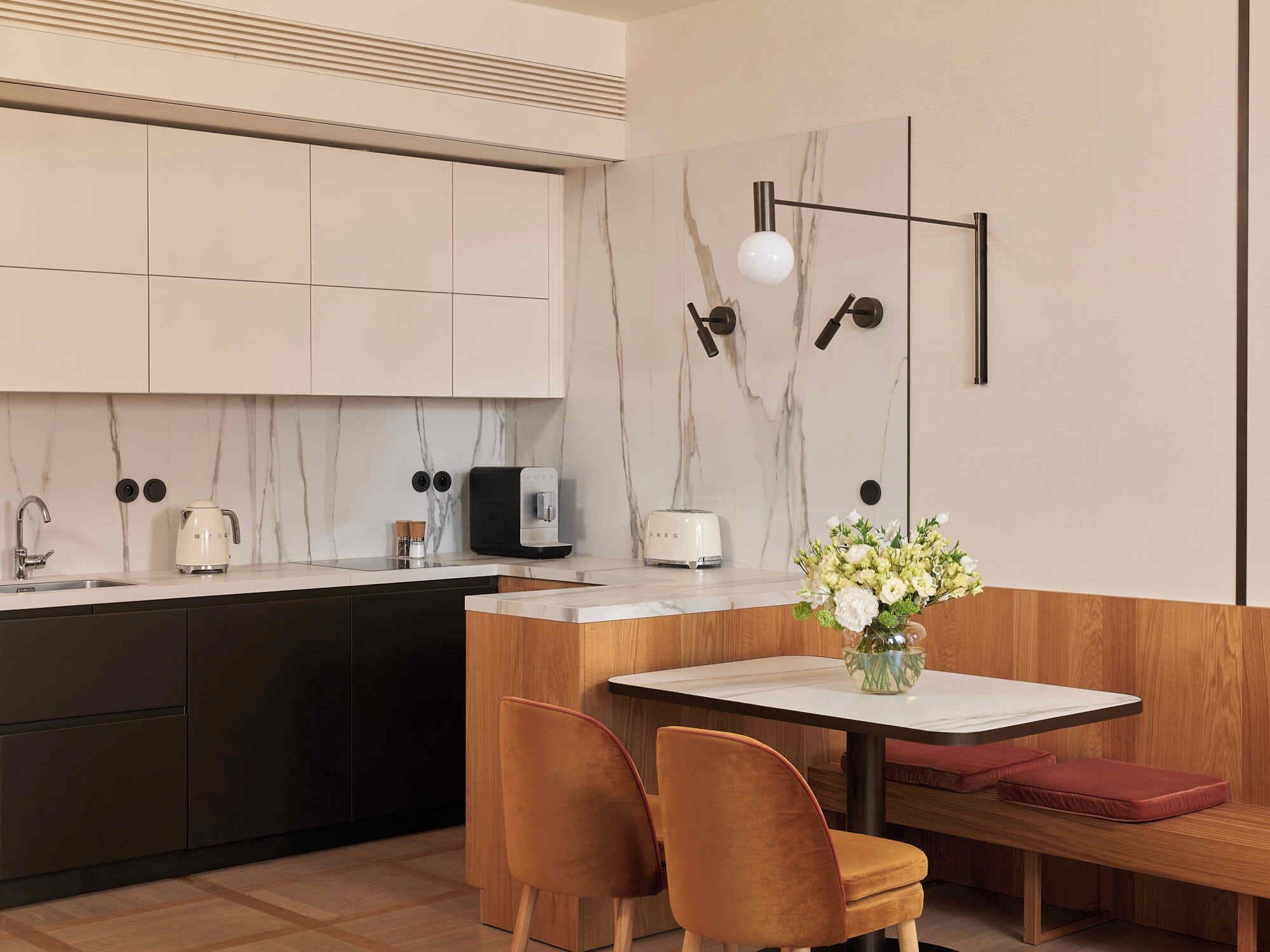 A modern kitchen with a marble backsplash, a built-in coffee maker, a toaster, and a wooden dining area with a bench and chairs.