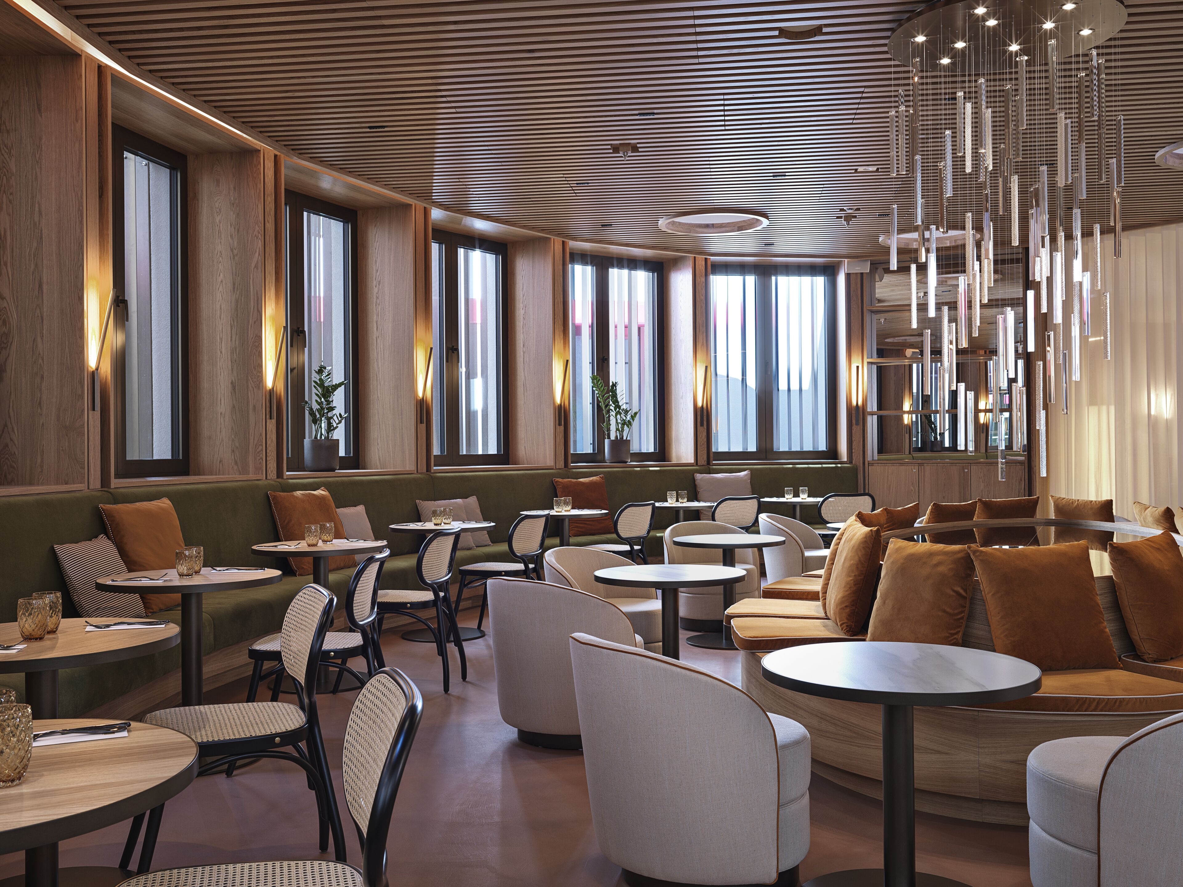 A modern restaurant interior with wooden panel walls, large windows, and a variety of seating options including tables and couches.