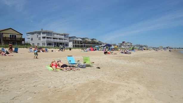 Une plage avec de nombreuses chaises longues et des parasols, un poste de surveillance pour les sauveteurs, et un grand bâtiment doté de plusieurs balcons.