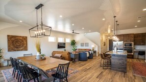 A spacious living area with a wooden dining table, black chairs, and a large sofa. There is a kitchen area with modern appliances and a bar counter. - Arcadia 50 | Shuffleboard * Sleeps 22 * Views of Red Rocks (Santa Clara)