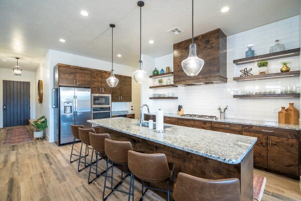 A modern kitchen with a central island, bar stools, wooden cabinets, and pendant lighting.
