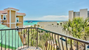 Varanda com vista para uma praia, palmeiras e um barco ao longe.