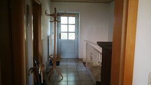 Ein schmaler Flur mit Heizkörper, Holz-Kleiderhaken und einer Tür zu einem Zimmer.