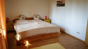 Ein Schlafzimmer mit einem hölzernen Bett, zwei Nachttischen, einem kleinen Tisch, einer Lampe, einem Bild an der Wand und einem Holzboden.