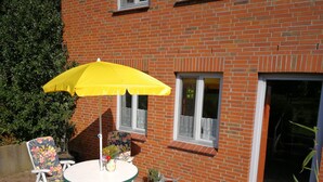 Eine Terrasse mit Tisch und Stühlen, einem gelben Sonnenschirm und einem Ziegelgebäude mit Fenstern.